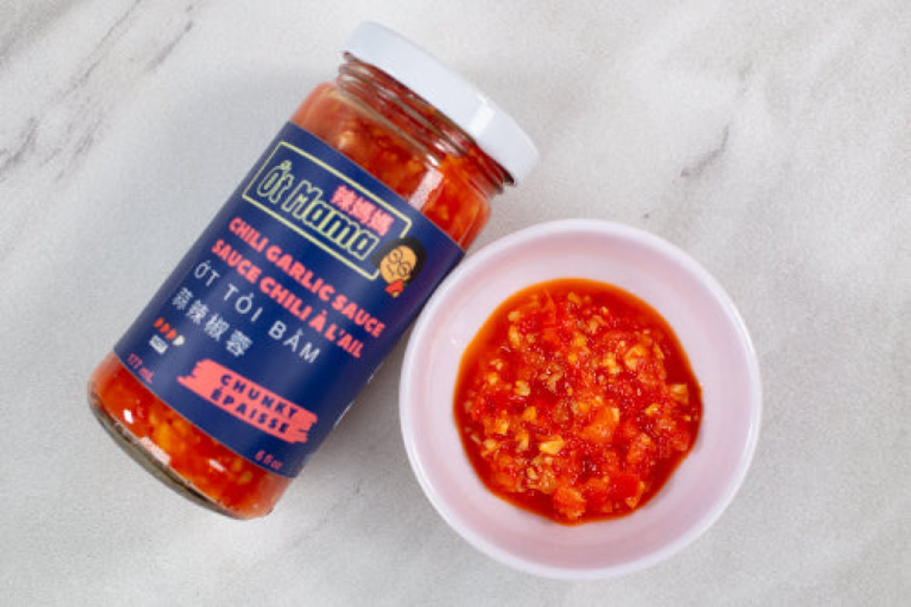 Bottle of chili garlic sauce with a small bowl of the sauce on a marble surface